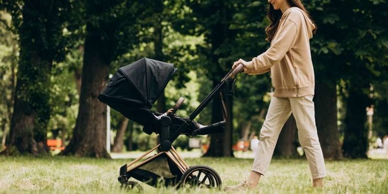 Young mother walking with baby carriage in park off road stroller